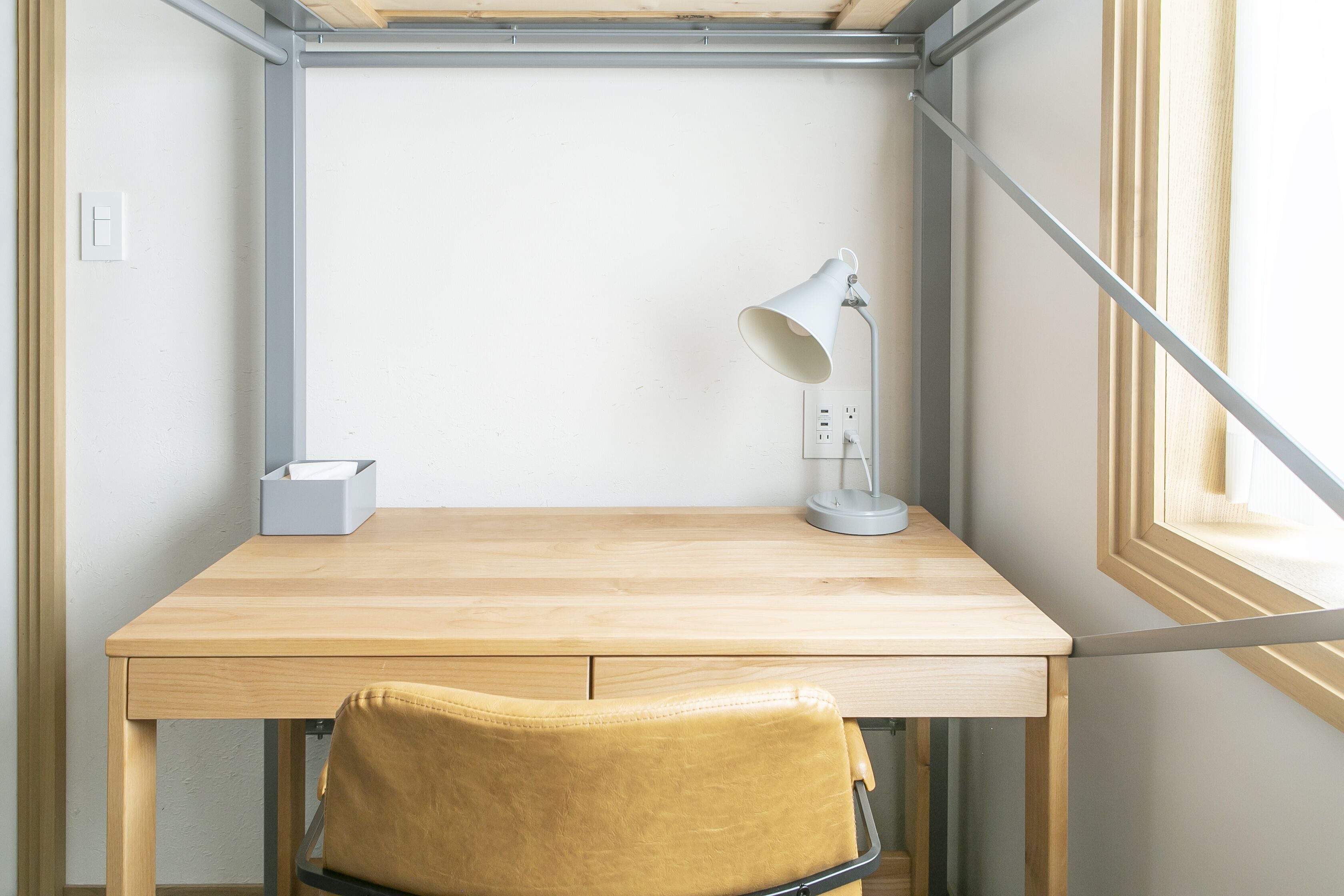 A wooden desk with a lamp, a chair, and a power outlet.