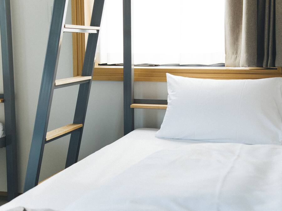 A single bed with a white pillow and a wooden headboard in a room with a window and curtains.