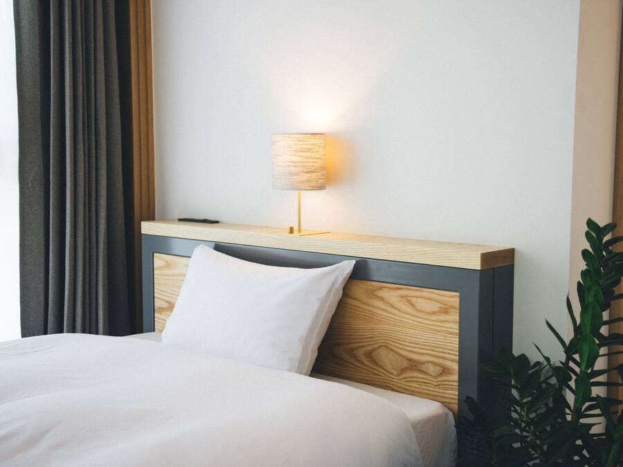 A neatly made bed with a wooden headboard, a bedside lamp, and a potted plant beside the bed.