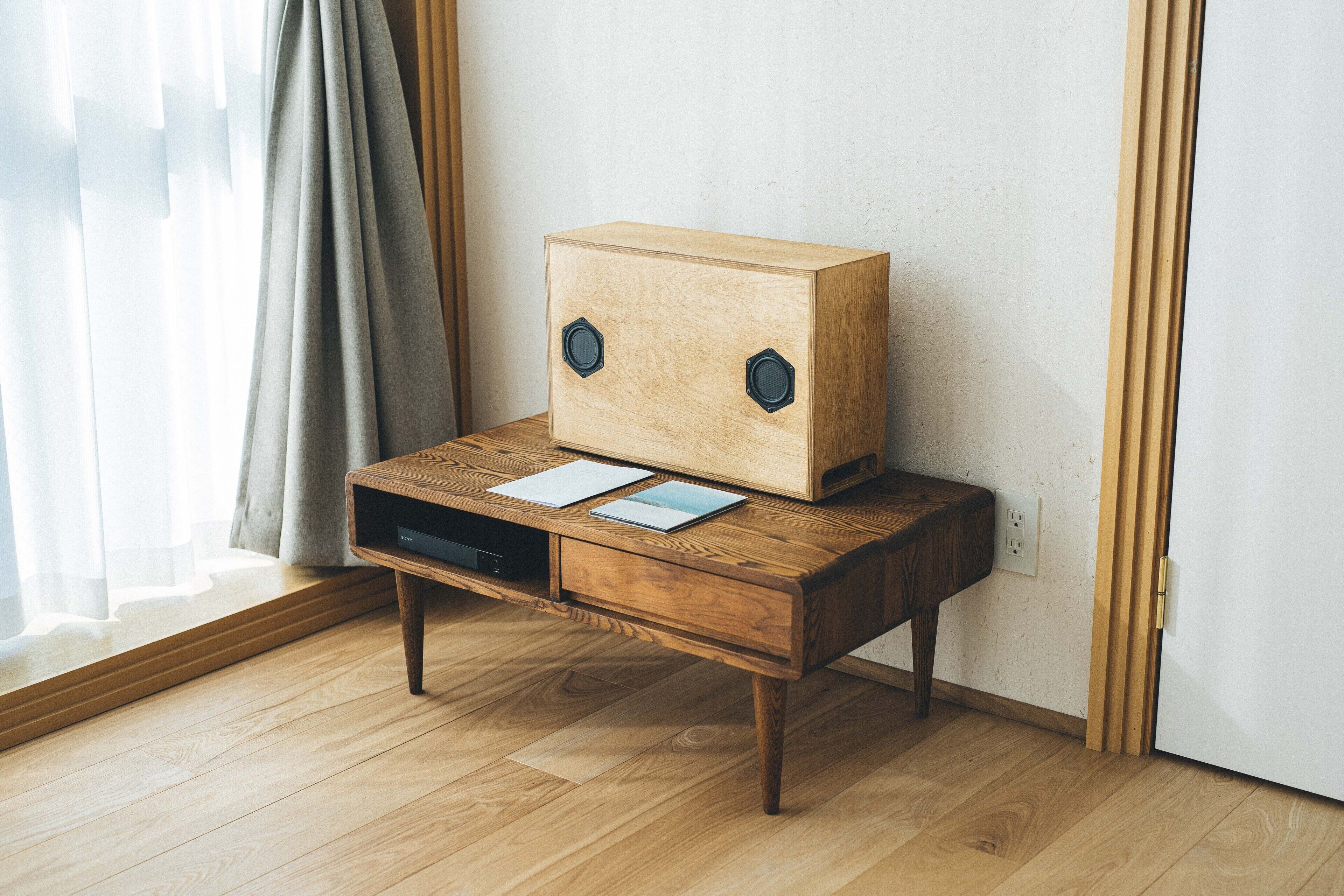 A wooden desk with a unique head-shaped object on top, two drawers, and a window with curtains.