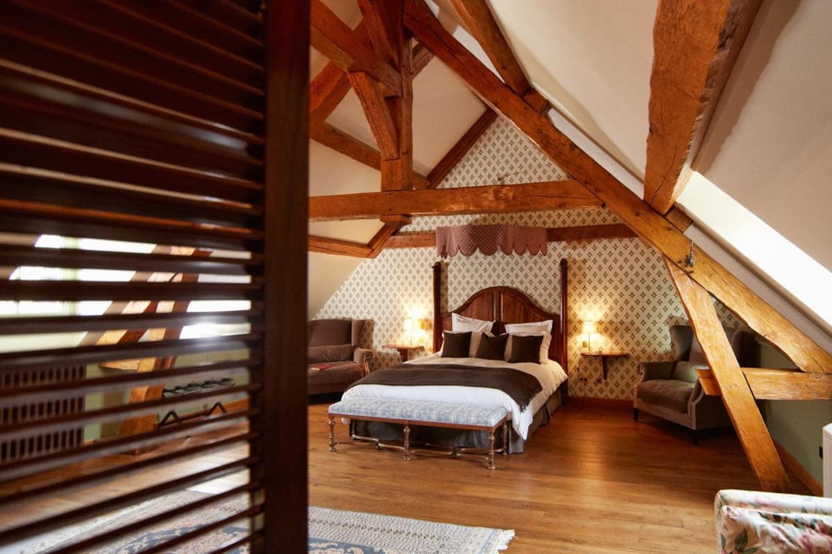A bedroom with a wooden ceiling, a bed with a headboard, two bedside tables, and a chair.