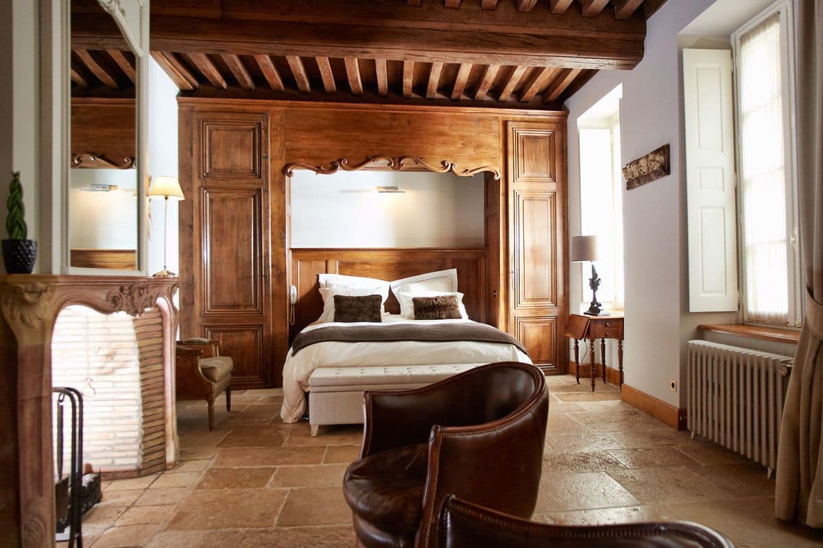 A bedroom with a large bed, wooden ceiling beams, a radiator, and a window.
