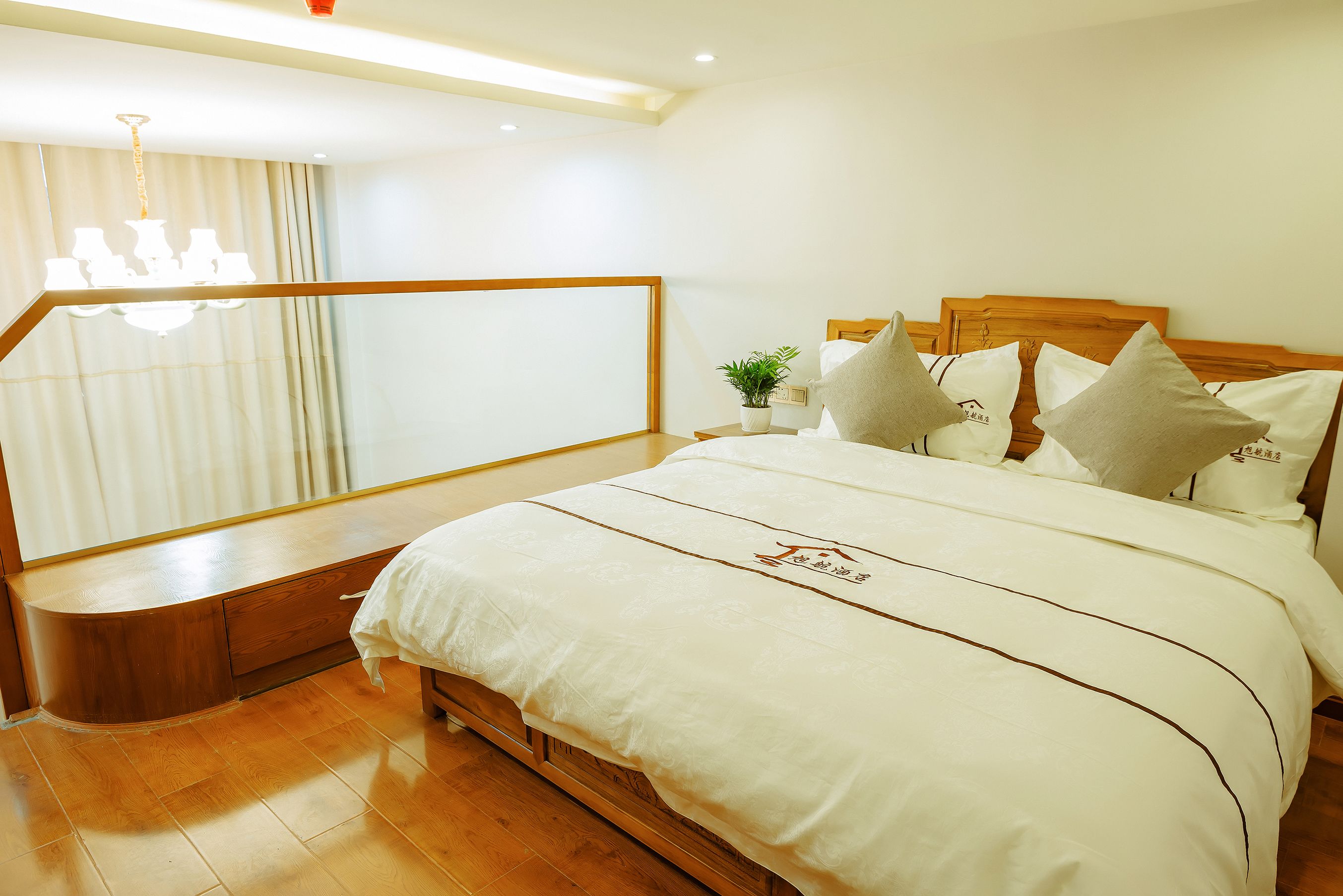 Un dormitorio ordenado con una cama de madera, una mesita de noche con una planta y vistas al exterior a través de una ventana con cortinas.