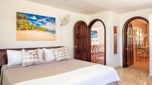 Een hotelkamer met een groot bed, een strandafbeelding, een ventilator en uitzicht op het strand door een geopende deur.