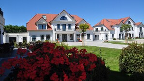 Une rangée de bâtiments blancs aux toits rouges, une pelouse bien entretenue et des fleurs rouges au premier plan.