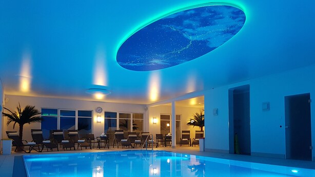 Une piscine intérieure dotée de chaises longues et d’un plafond décoré d’un motif de ciel étoilé.