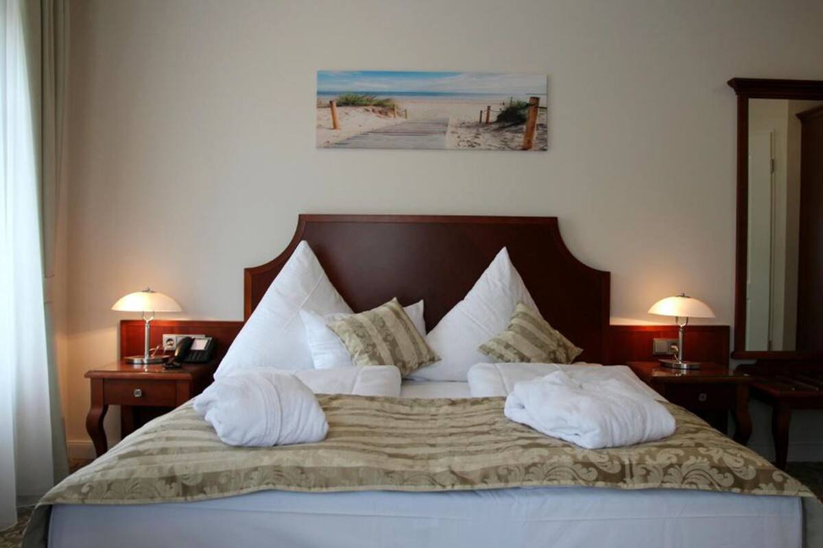 A neatly made bed with white and patterned pillows, a beige and green striped blanket, and two bedside lamps.