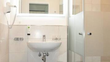 A bathroom with a white sink, a mirror, a glass shower enclosure, and a small stool.