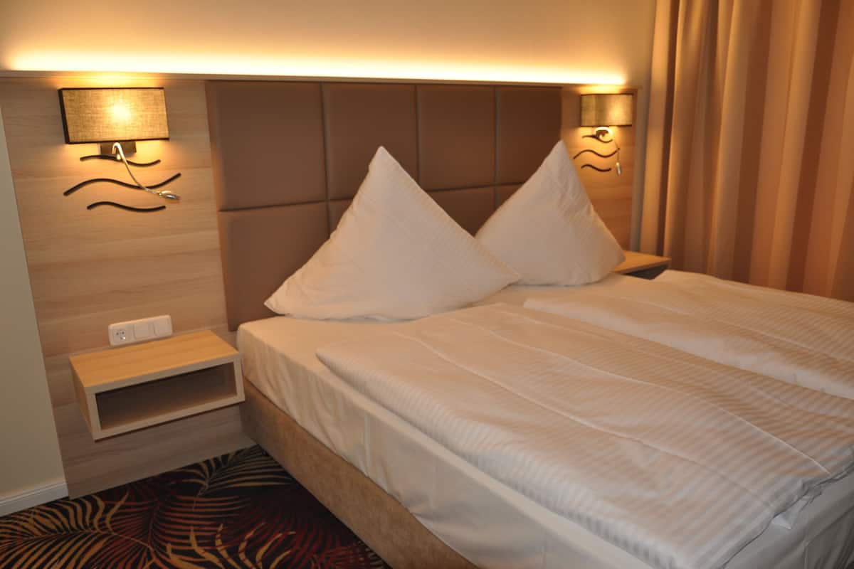A hotel room with a bed, a nightstand, a wall-mounted lamp, and a power outlet.