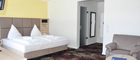 Una habitación de hotel con cama, una silla, una mesita y una puerta que da a otra estancia.