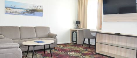 A hotel room with a sofa, a small table, a desk, a TV, and a patterned carpet.