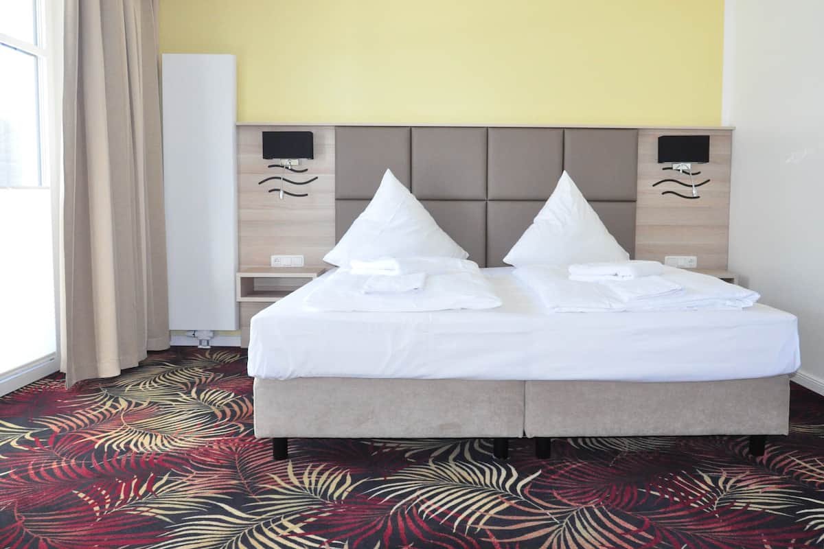 A hotel room with a bed, a flat-screen TV, a headboard with a wave design, and a patterned carpet.