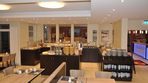 Un espace de restauration moderne dans un hôtel, comprenant un buffet, des tables et des chaises, ainsi qu'un comptoir d'accueil.