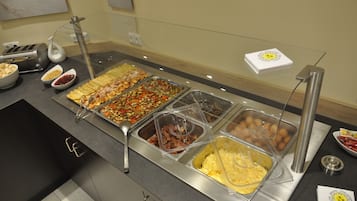 Un bufé con diversas opciones de comida, que incluyen carnes, verduras y postres, servidos en recipientes transparentes.