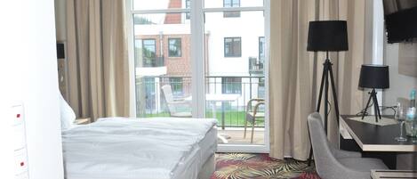 Une chambre d’hôtel avec un lit, un bureau avec une lampe, une chaise et un balcon donnant sur des immeubles.