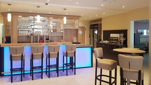 Un espace bar moderne comprenant un comptoir, de nombreux tabourets et un coin salon avec une table ronde et des chaises.