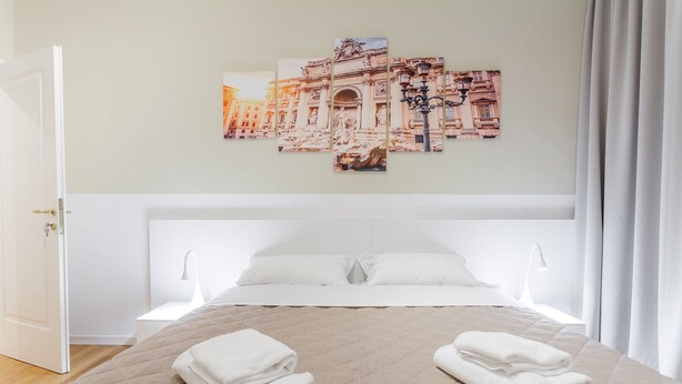 A hotel room with a large bed, white bedding, a view of a historic building, and a neatly folded towel on the bed. - Maison Giulivia a San Pietro (Rome)