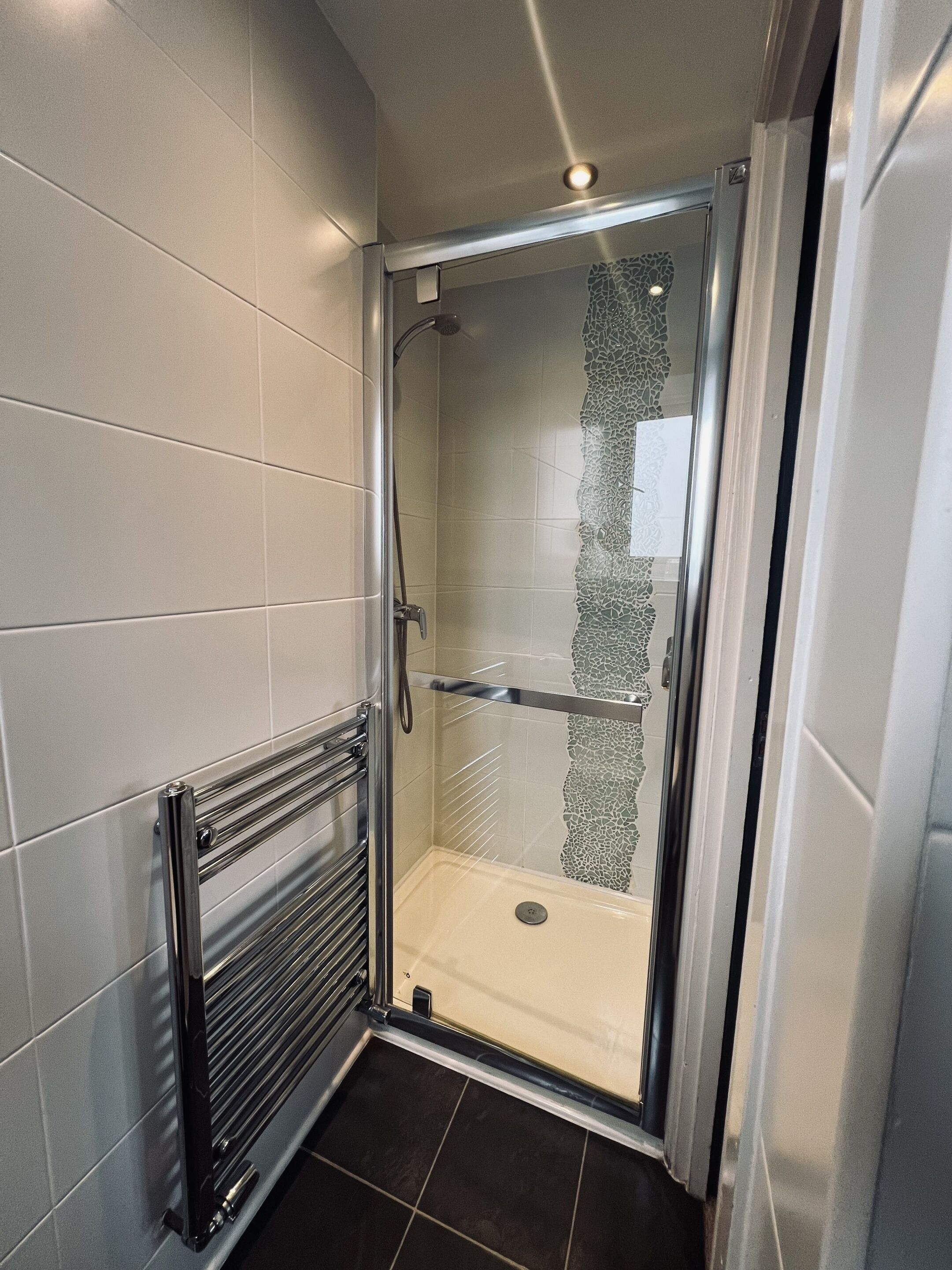 A modern shower with a glass door, a metal towel rack, and a tiled floor.