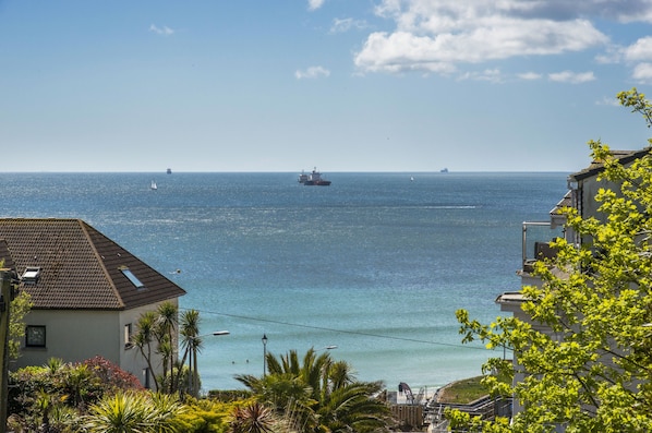 A coastal view with a building, clear sky, and a ship in the distance.