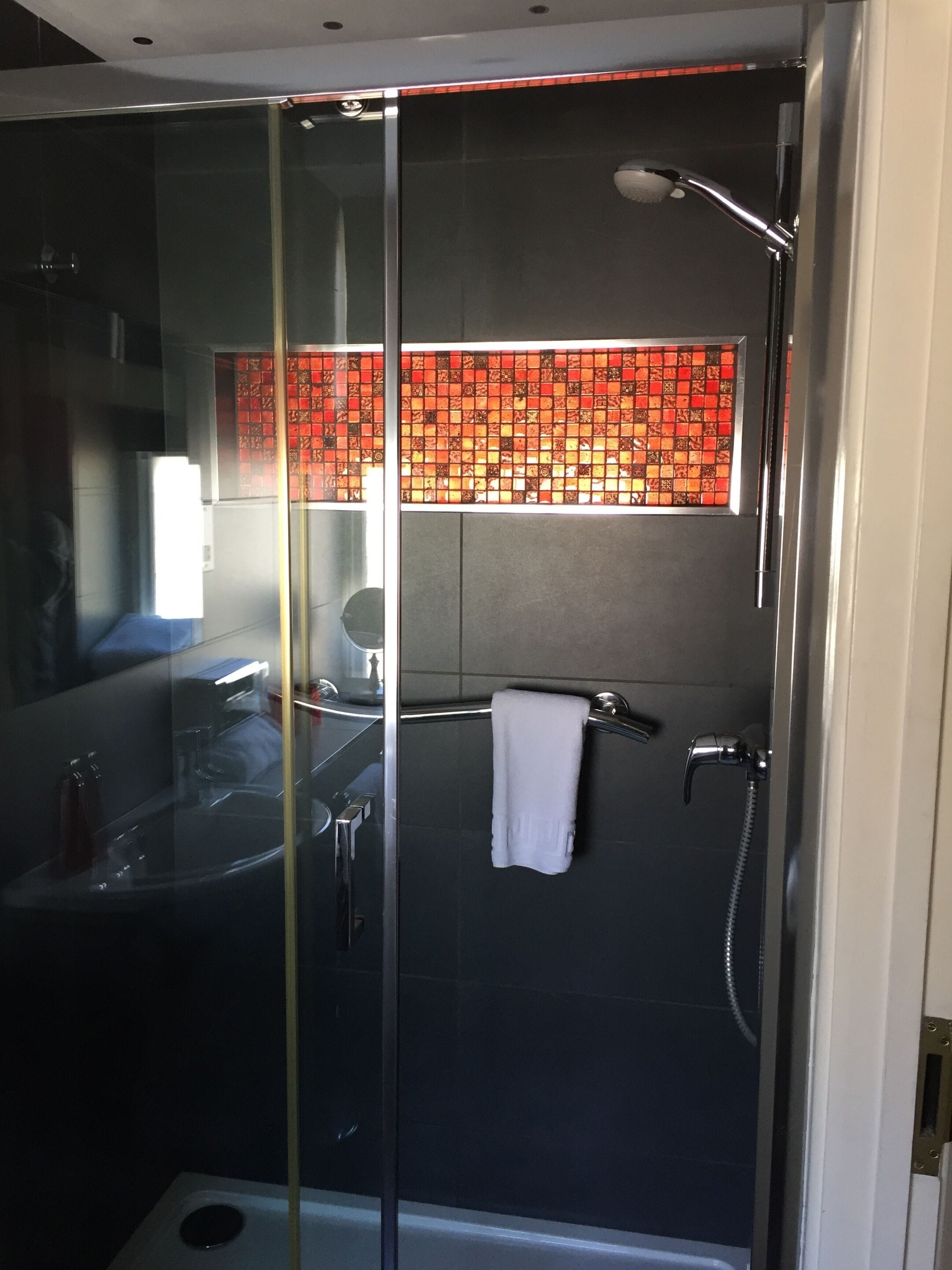 A modern bathroom with a glass-enclosed shower, a visible bathtub, and a towel hanging on the wall.