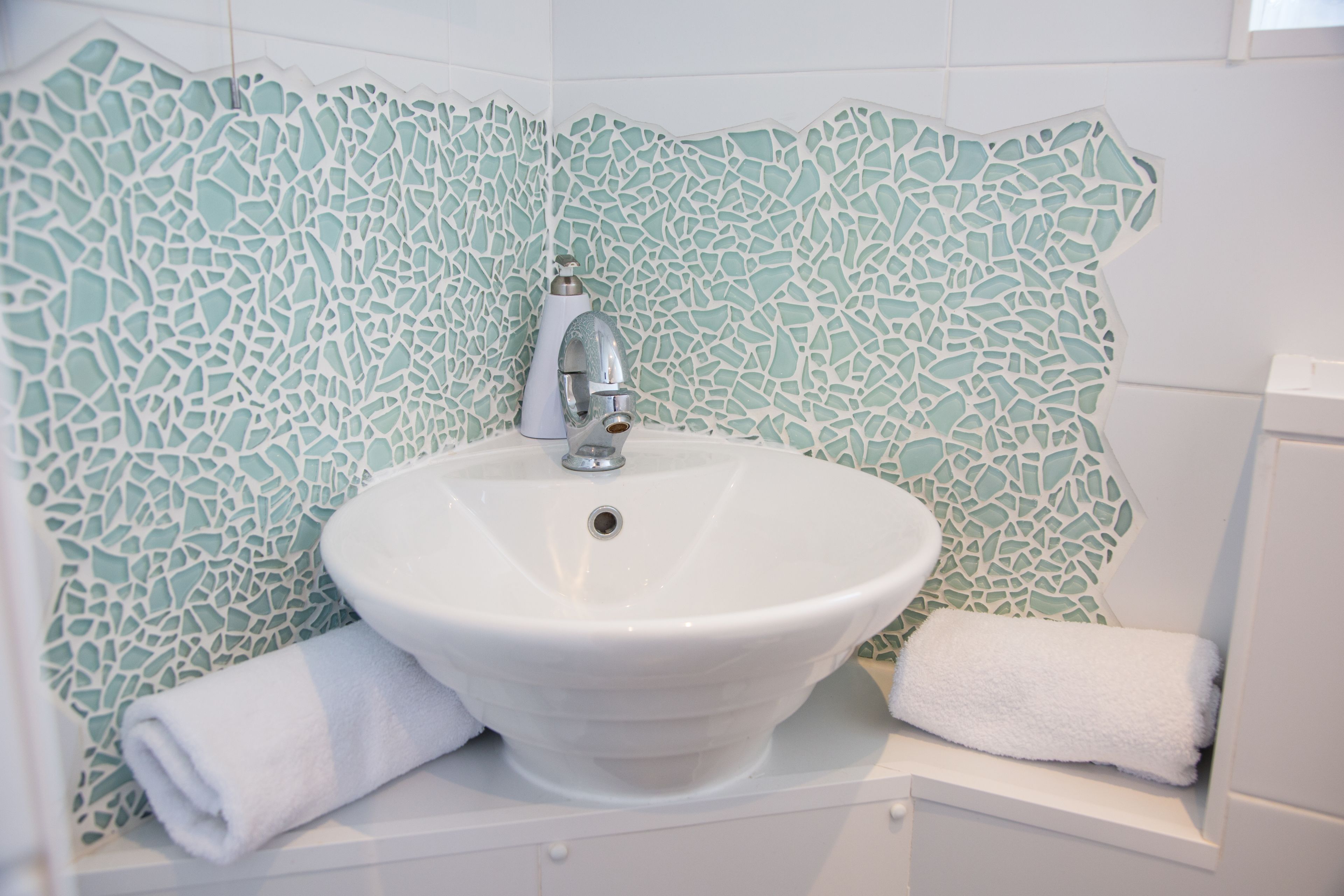 A bathroom with a white sink, a faucet, and a decorative mosaic tile wall.