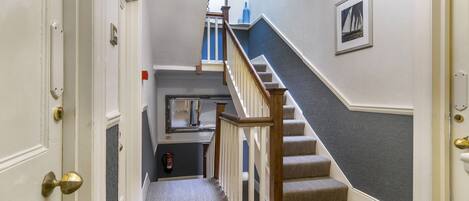A hallway with a carpeted floor, a wooden staircase with a white railing, and a door with a brass doorknob.