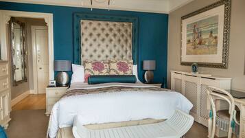 A bedroom with a large bed, two bedside tables with lamps, a dresser, a chair, and a framed painting on the wall.