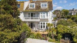 Een huis met twee verdiepingen en een balkon, omringd door weelderige begroeiing.