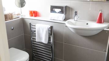 Ein Badezimmer mit einer weißen Toilette, einem Handtuchhalter mit einem weißen Handtuch, einem Waschbecken mit einem roten Seifenspender und einem Spiegel.