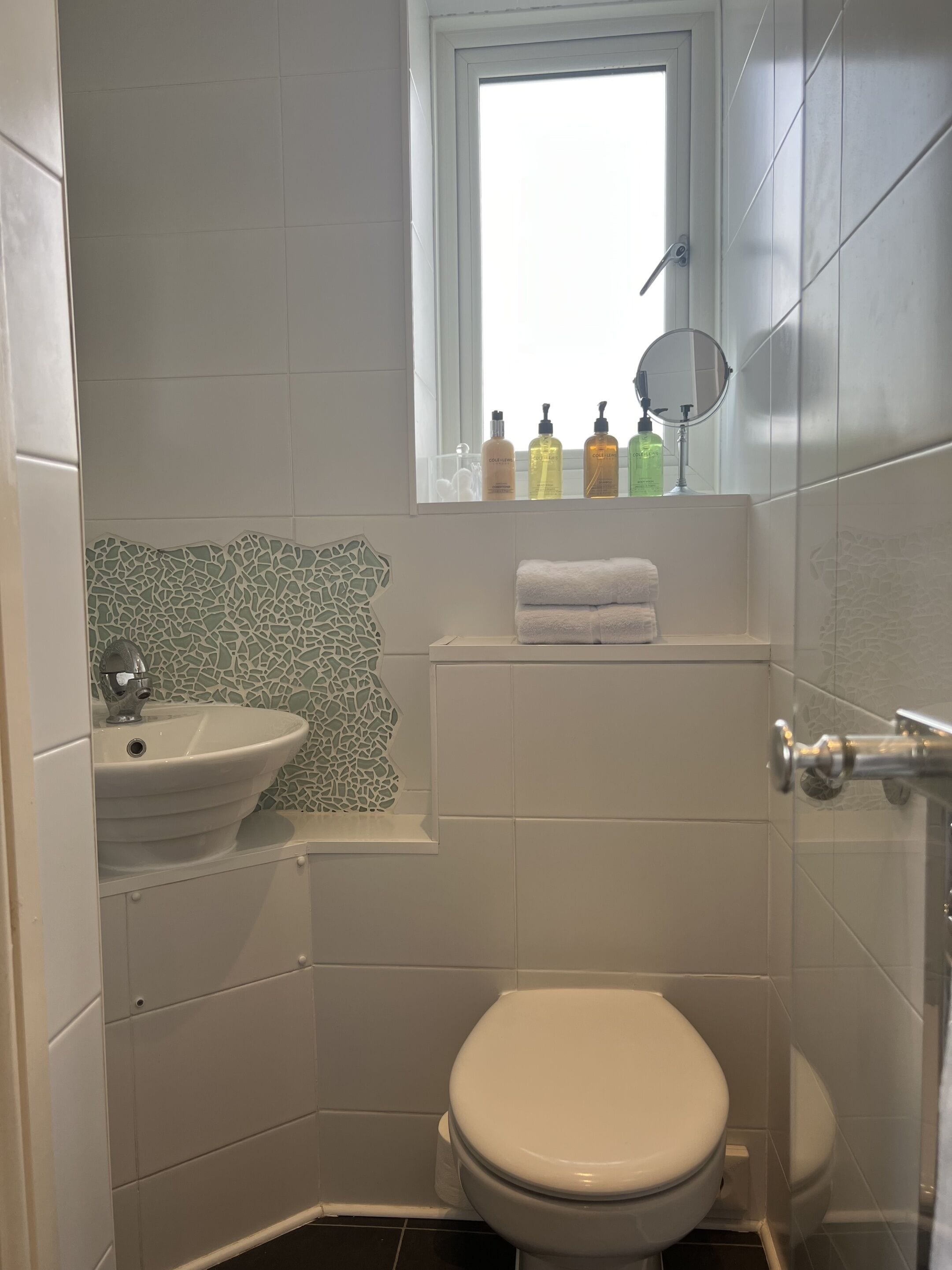 Un baño pequeño y funcional con un lavabo blanco, inodoro y una ventana sobre el inodoro.
