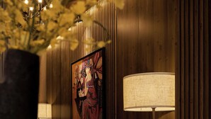A hallway with wooden paneling, a floor lamp, a table with a vase of flowers, and a framed artwork on the wall. - The One Premium Hotel (Ho Chi Minh City)