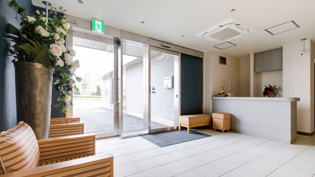 A reception area with a glass door entrance, a reception desk, and seating area with striped cushions. - Kansai Seaside Hotel (Kaizuka)