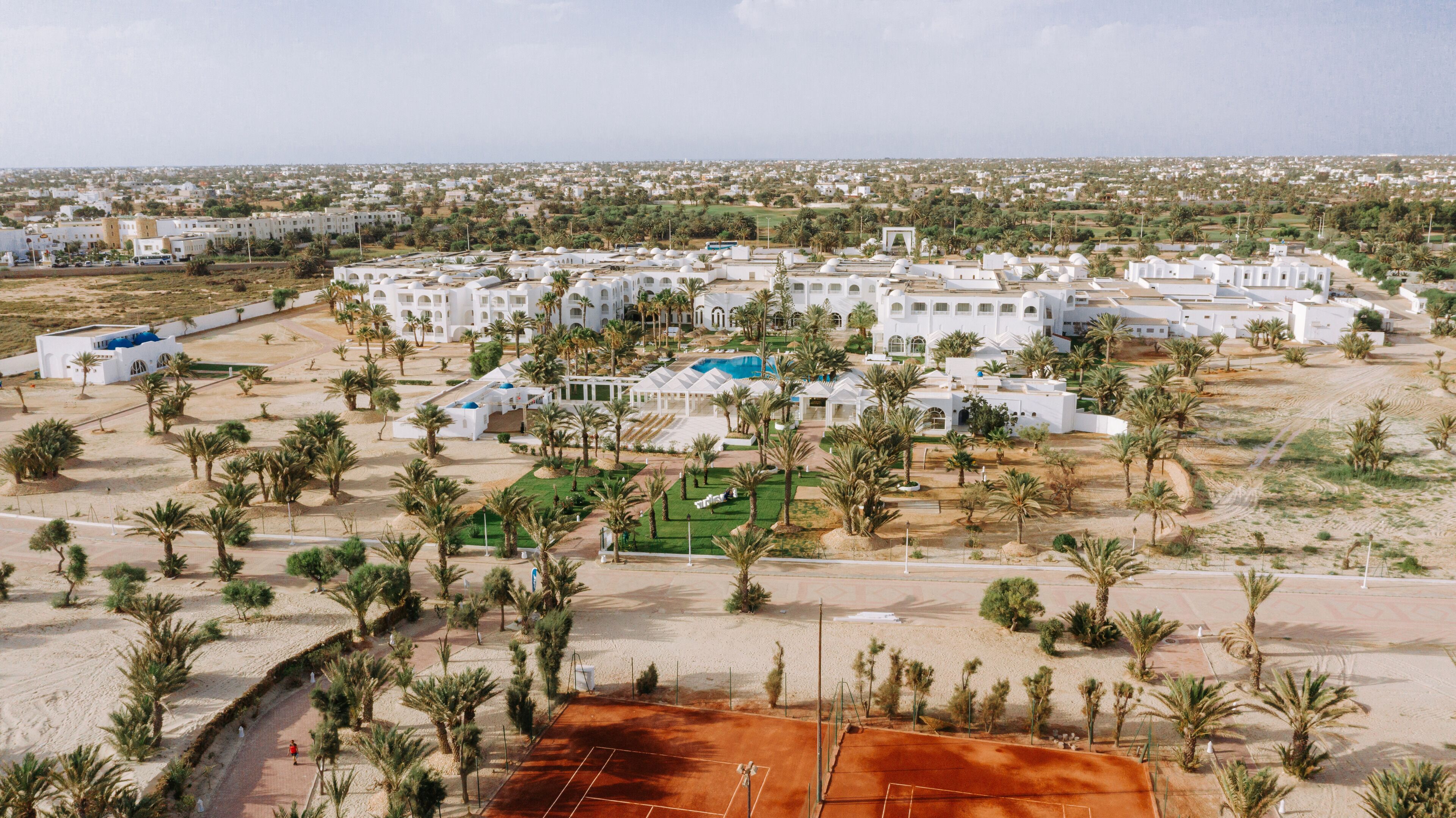 A large resort with multiple white buildings, palm trees, and a tennis court.