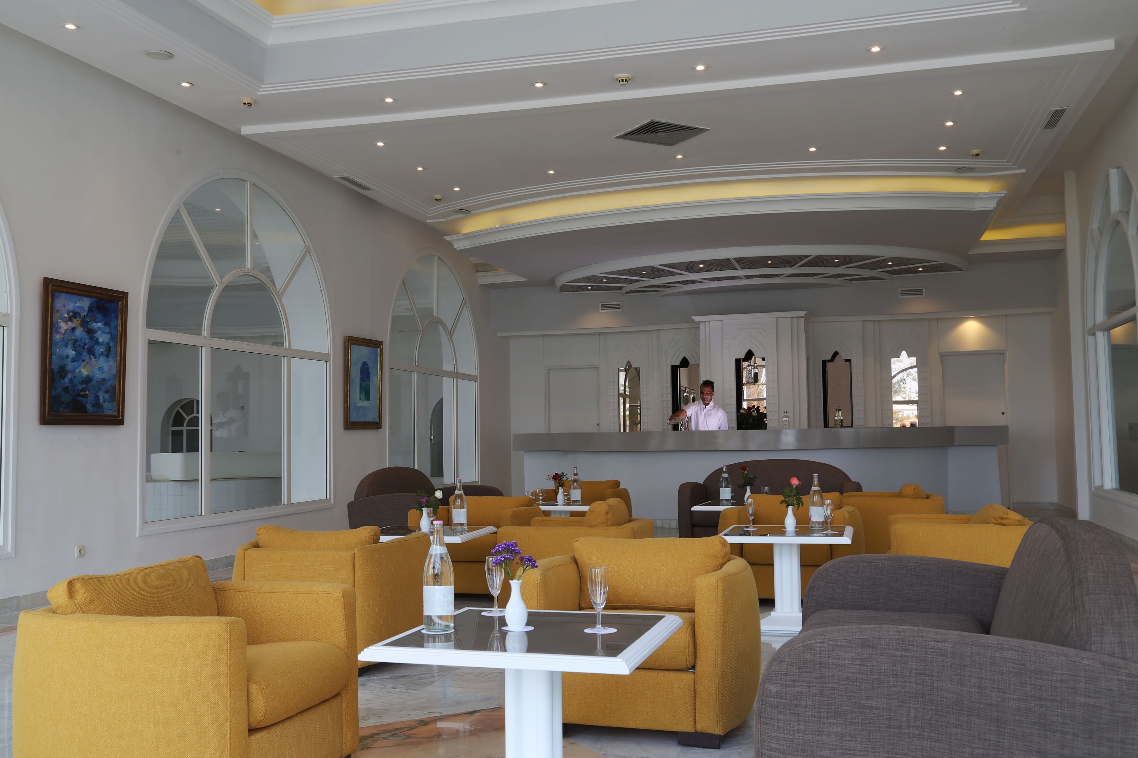Un hall d’hôtel moderne avec des canapés jaunes, des tables blanches et de grandes fenêtres.