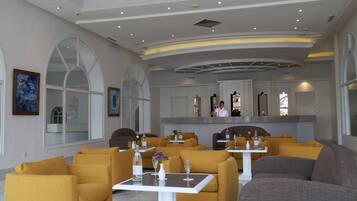 Un hall d’hôtel moderne avec des canapés jaunes, des tables blanches et de grandes fenêtres.