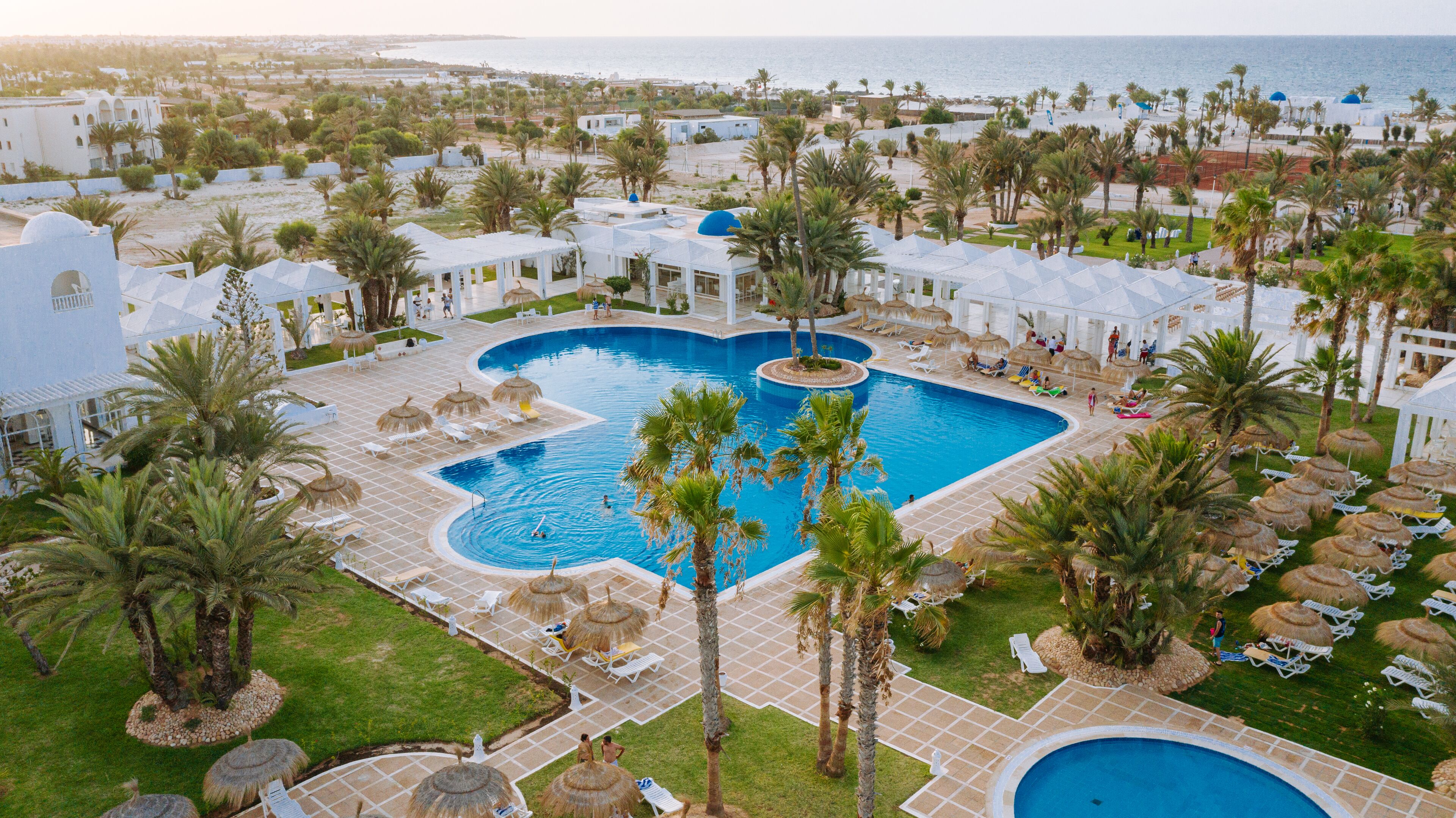 Een resort met een centraal gelegen zwembad, palmbomen en strandparasols.