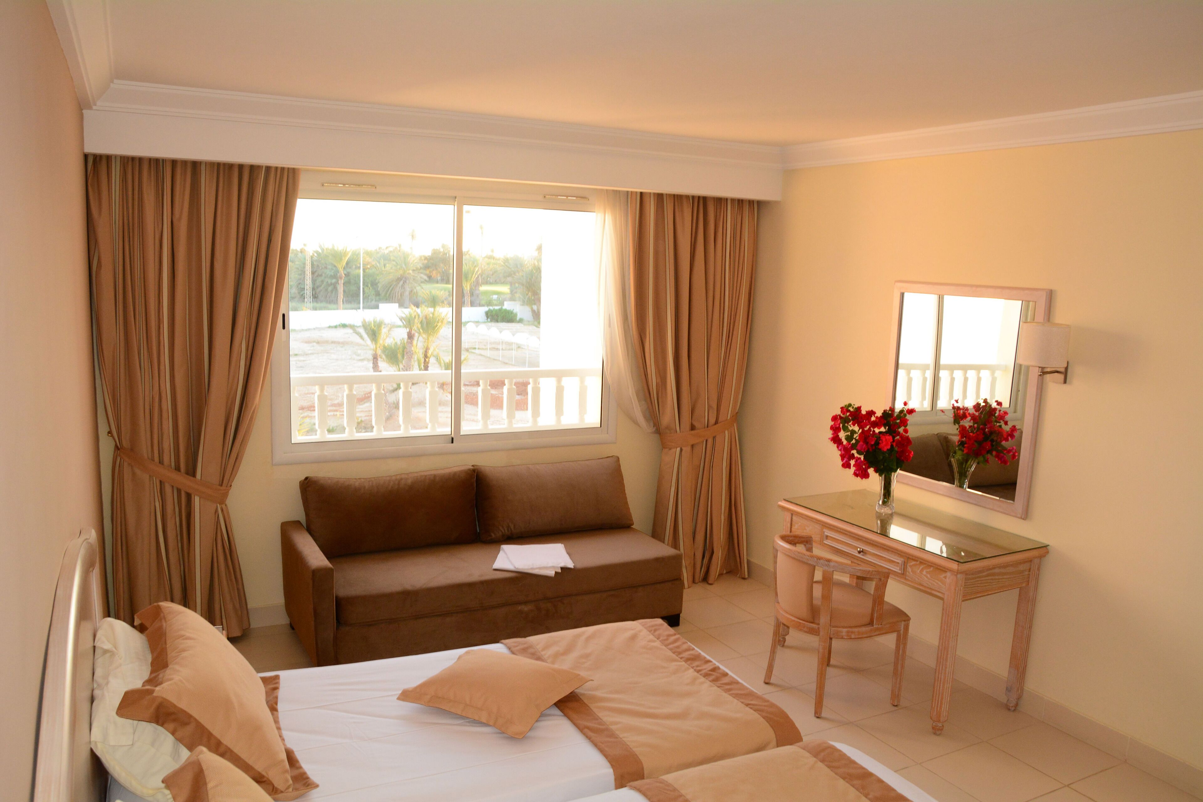 A hotel room with a bed, a sofa, a desk, and a window with curtains.