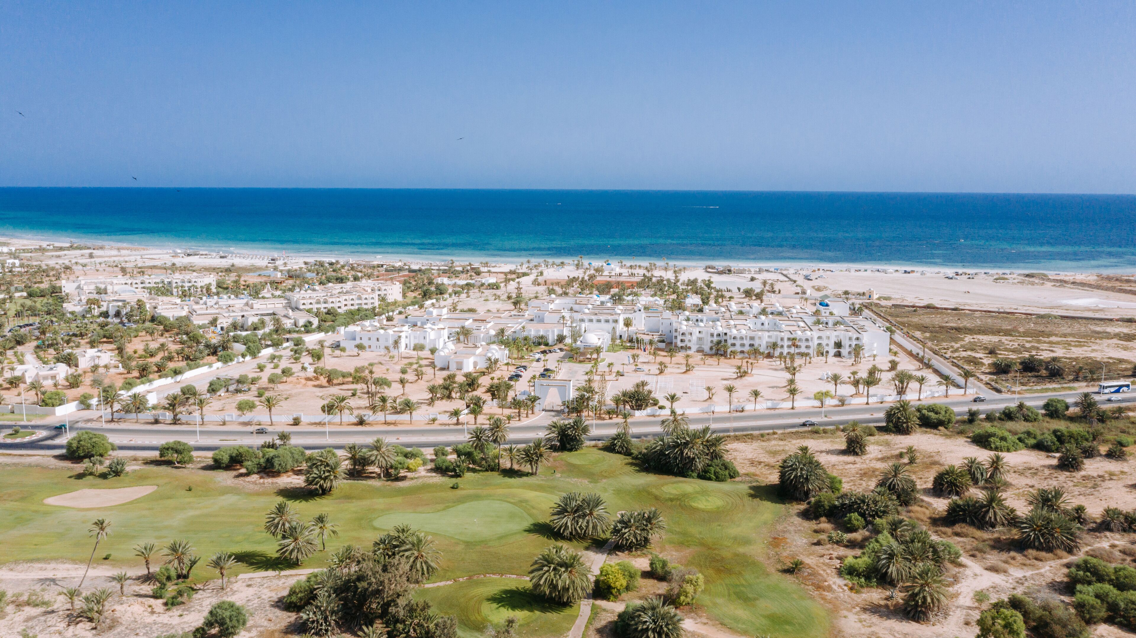 Vista aérea de un resort costero con edificios blancos, un campo de golf y una playa.