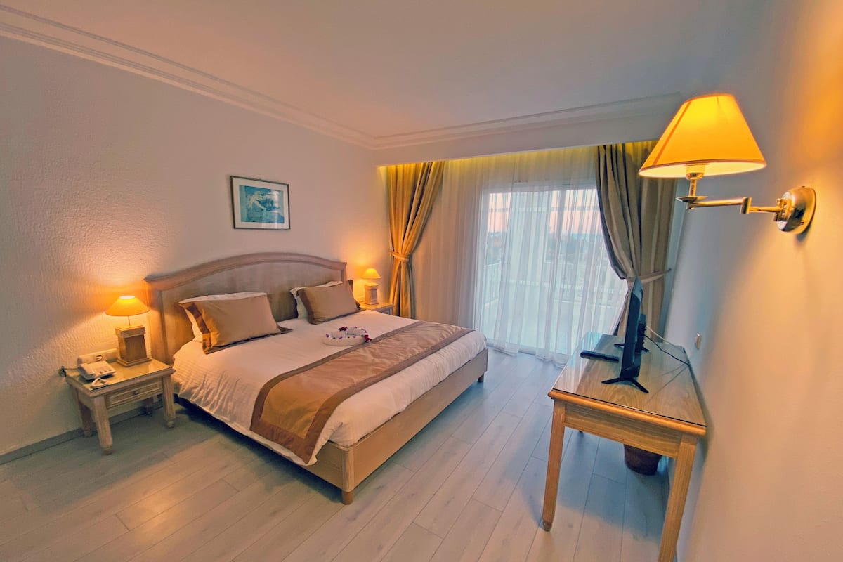 Une chambre d’hôtel avec un grand lit, des lampes de chevet, une table de chevet et une fenêtre avec des rideaux.