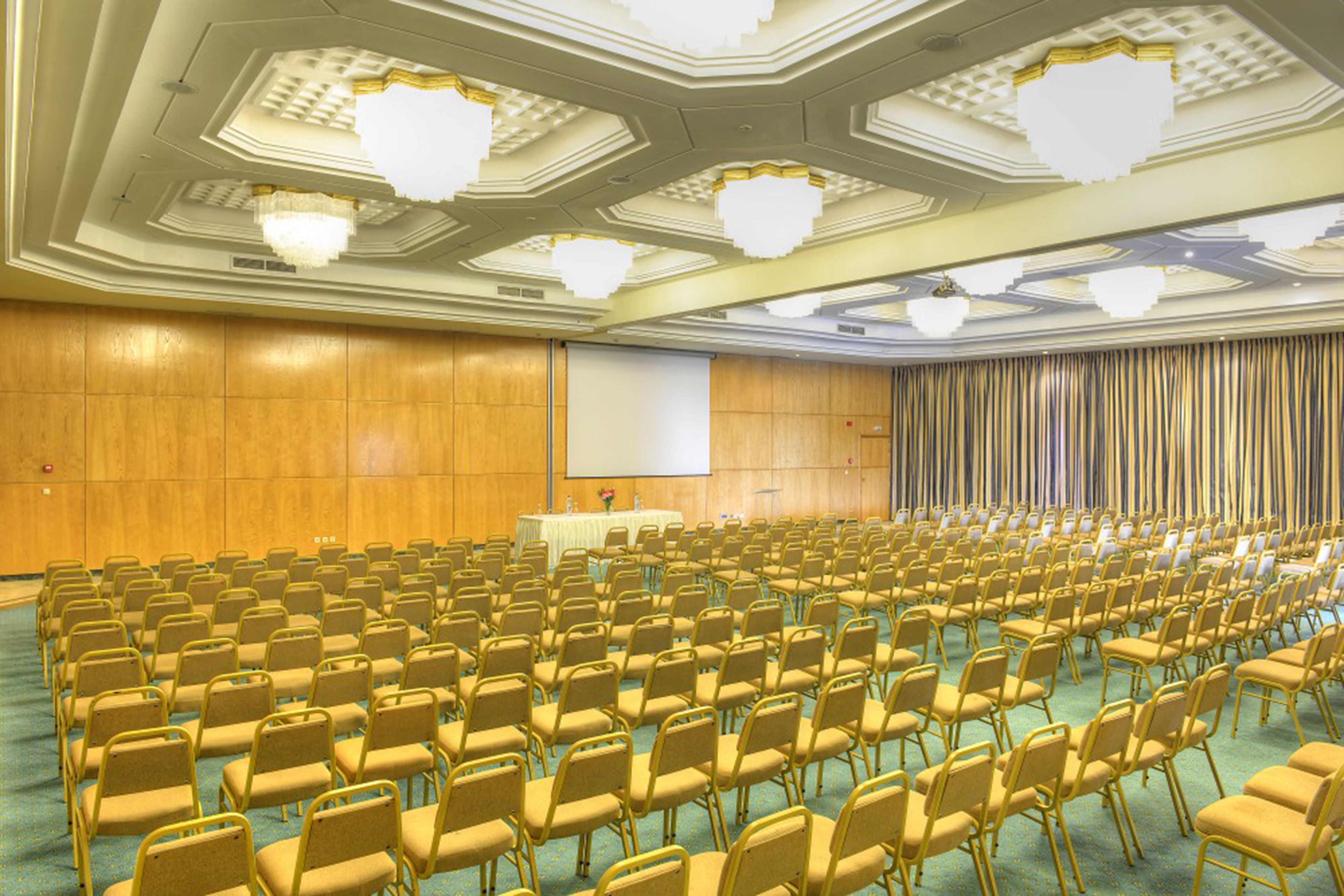 A conference room with rows of chairs, a podium, and a screen.