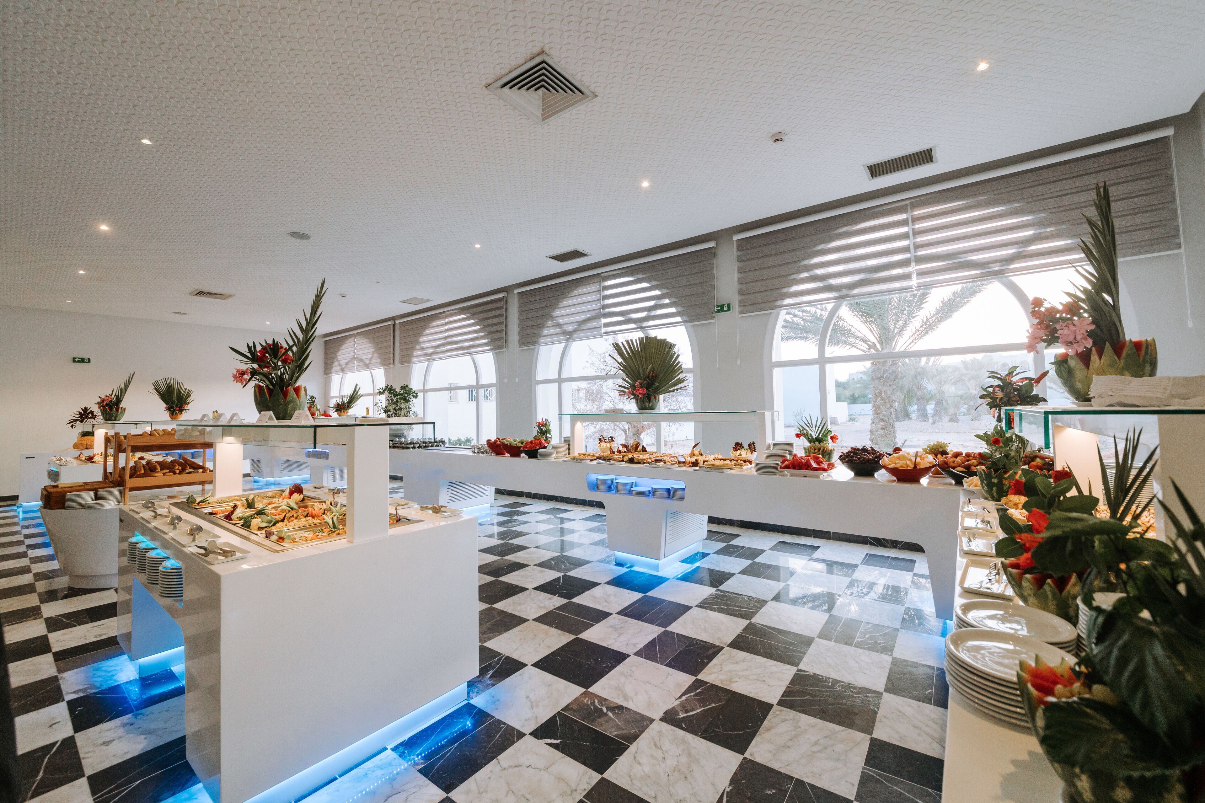 A buffet area with a checkered floor, buffet stations, and potted plants.
