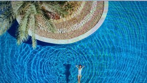 Une personne se tient debout dans une piscine circulaire bordée de petits galets et entourée de palmiers.