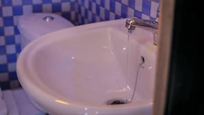 A bathroom sink with running water, a toilet, and blue and white checkered tiles on the wall.