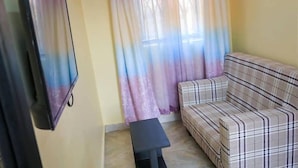 A living room with a plaid sofa, a small black table, and a TV mounted on the wall.