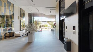 A modern hotel lobby with a central white floral arrangement, a seating area, and a reception desk.