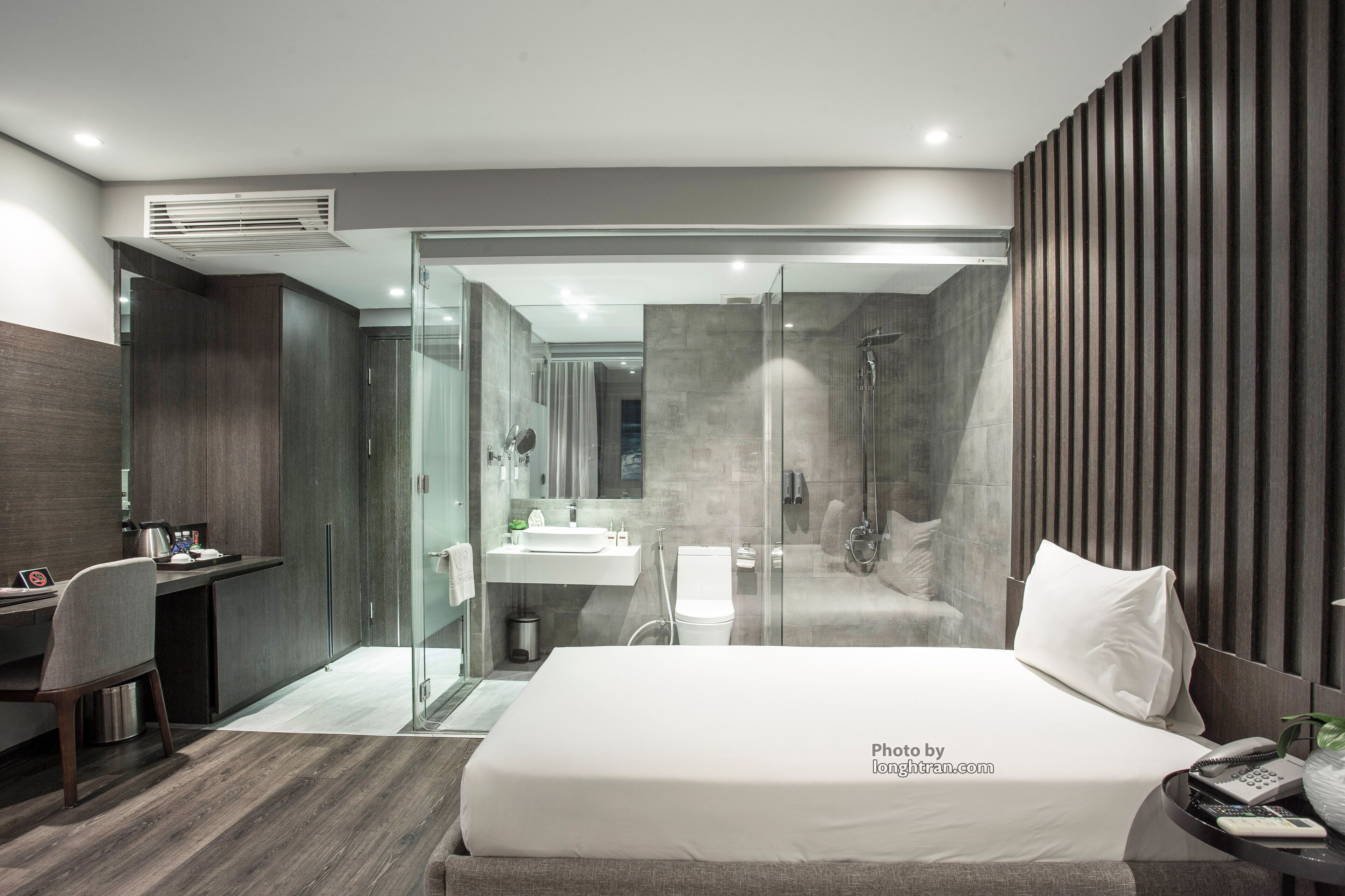 A modern hotel room with a bed, desk, and shower area.