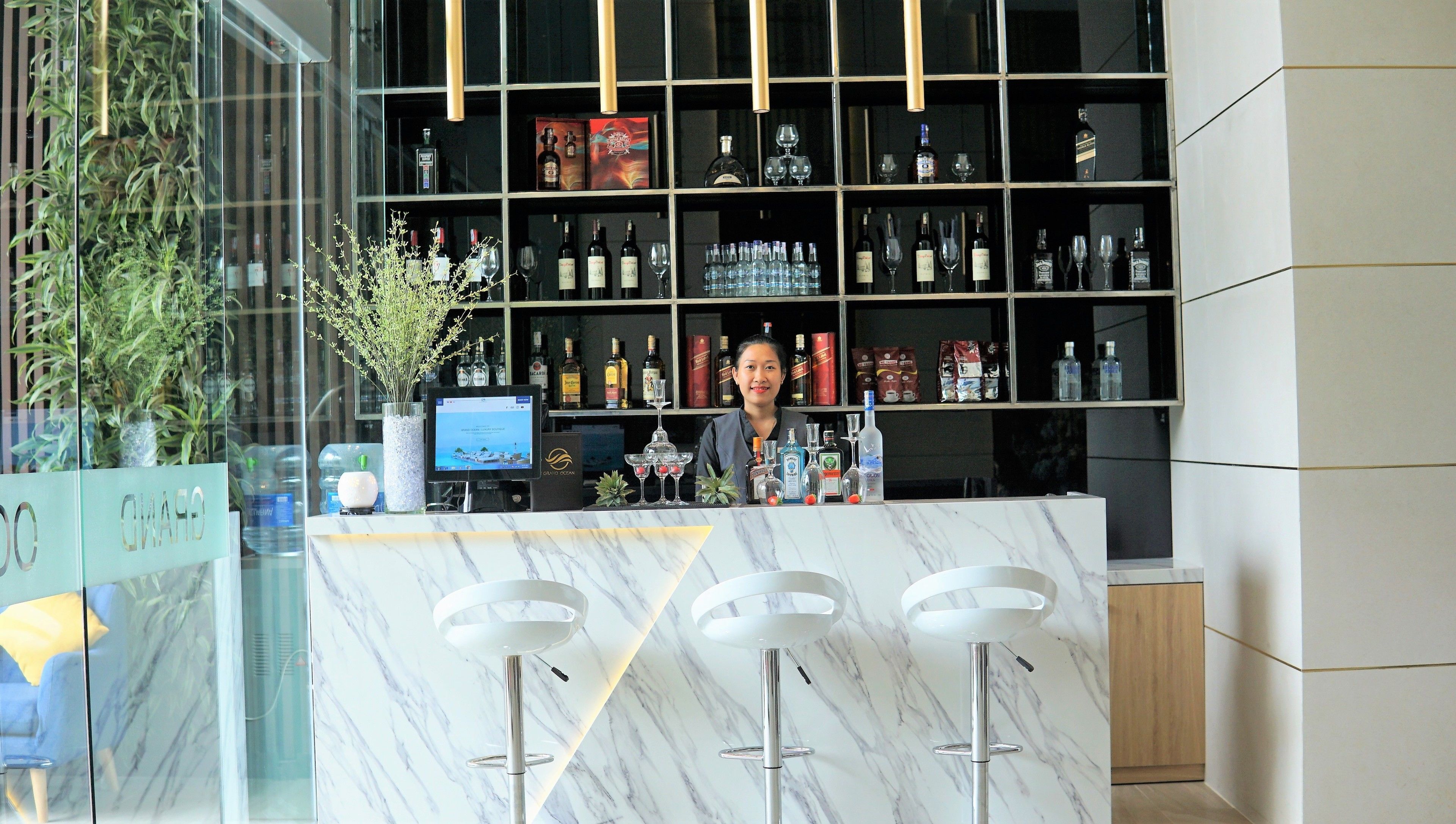 Un espace bar doté d’un comptoir en marbre, de nombreuses bouteilles d’alcool et d’un écran numérique.