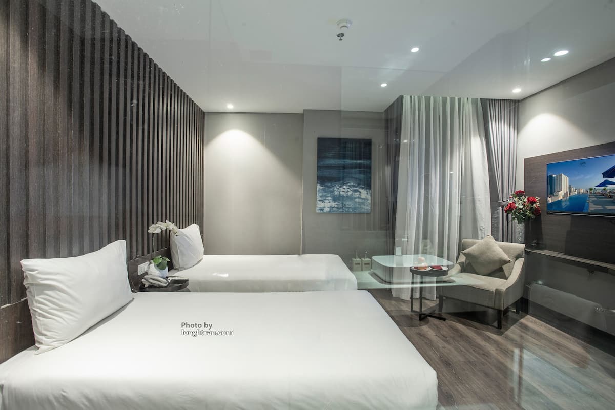 Una habitación de hotel moderna con dos camas, una mesa de centro de vidrio, un sofá y un televisor.