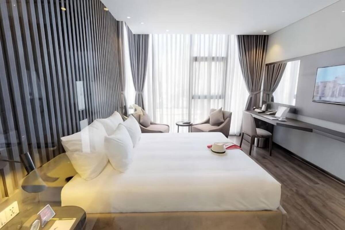 Una habitación de hotel moderna con una cama grande, un escritorio, una silla y una mesita.