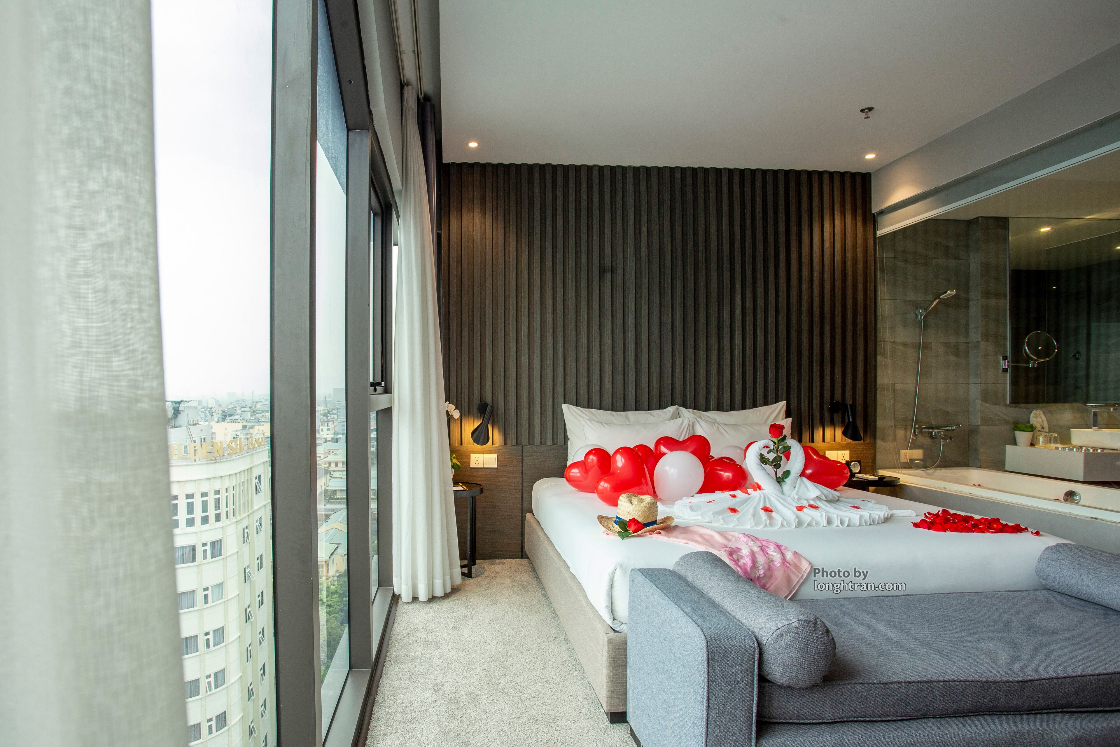 Une chambre d’hôtel moderne dotée d’un grand lit, offrant une vue sur la ville, comprenant une salle de bain avec une douche en verre et un balcon avec des rideaux.